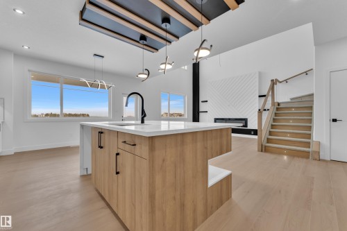 Kitchen featuring hanging light fixtures, modern cabinets, a center island with sink, light stone countertops, and light wood finished floors - 202 Basin Court, Leduc, AB - Indoor Photo Showing Kitchen With Upgraded Kitchen