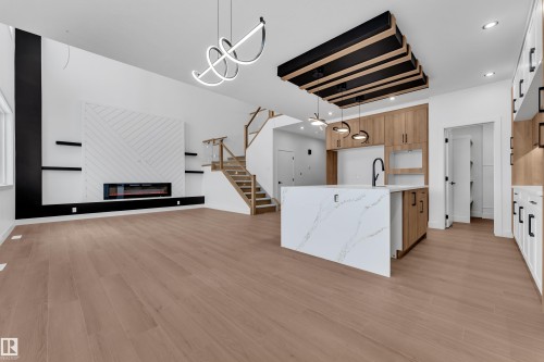 Kitchen with light stone counters, an island with sink, open floor plan, a glass covered fireplace, and light wood-style flooring - 202 Basin Court, Leduc, AB - Indoor Photo Showing Kitchen