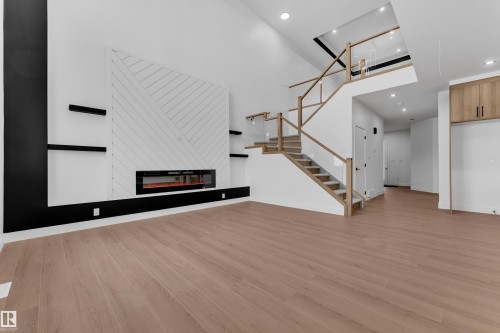 Unfurnished living room with a fireplace, a high ceiling, light wood-style flooring, and recessed lighting - 202 Basin Court, Leduc, AB - Indoor With Fireplace