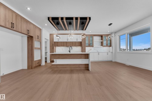 Kitchen with pendant lighting, light wood-style flooring, a center island with sink, open shelves, and light stone countertops - 202 Basin Court, Leduc, AB - Indoor Photo Showing Kitchen
