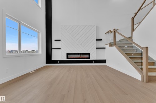 Unfurnished living room featuring a glass covered fireplace, light wood-style floors, healthy amount of natural light, and a high ceiling - 202 Basin Court, Leduc, AB - Indoor With Fireplace