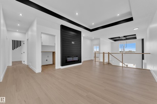 Unfurnished living room with a raised ceiling, a fireplace, recessed lighting, light wood-style flooring, and ornamental molding - 202 Basin Court, Leduc, AB - Indoor Photo Showing Other Room