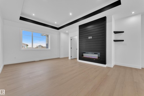 Unfurnished living room featuring a raised ceiling, light wood-style flooring, recessed lighting, a large fireplace, and ornamental molding - 202 Basin Court, Leduc, AB - Indoor