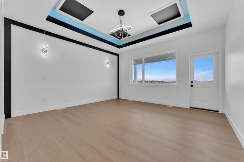 Empty room with a raised ceiling, hanging lights, and light wood-style floors - 202 Basin Court, Leduc, AB - Indoor Photo Showing Other Room