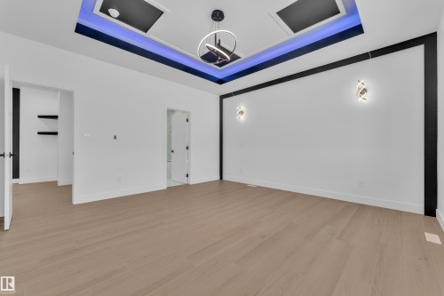 Empty room featuring a raised ceiling, light wood-type flooring, and suspended lighting - 202 Basin Court, Leduc, AB - Indoor Photo Showing Other Room
