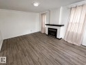 Spacious room featuring wood-finish flooring, a contemporary fireplace with a dark mantel, and multiple windows - 12235 104 Street, Edmonton, AB 