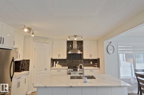 Kitchen featuring stainless steel appliances, light stone counters, white cabinets, an island with sink, and a textured ceiling - 315 Wild Rose Way, Edmonton, AB - Indoor Photo Showing Kitchen With Stainless Steel Kitchen With Upgraded Kitchen