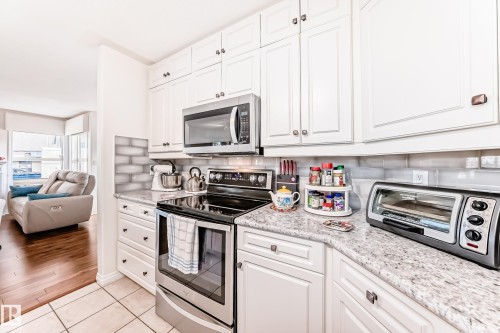 Kitchen with stainless steel appliances, white cabinets, open floor plan, light tile patterned flooring, and backsplash - 108 12028 103 Avenue, Edmonton, AB - Indoor Photo Showing Kitchen