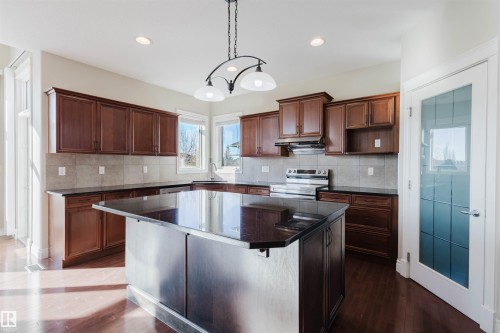 Kitchen featuring a kitchen breakfast bar, a center island, stainless steel electric stove, dark wood-type flooring, and backsplash - 3612 Mclay Court, Edmonton, AB - Indoor Photo Showing Kitchen With Double Sink