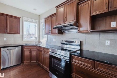 Kitchen featuring stainless steel appliances, tasteful backsplash, dark wood-style flooring, dark stone counters, and open shelves - 3612 Mclay Court, Edmonton, AB - Indoor Photo Showing Kitchen