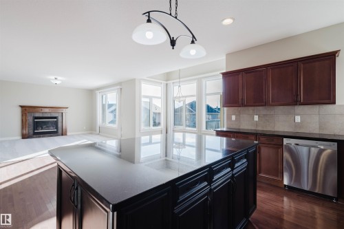 Kitchen with a kitchen island, a fireplace, dishwasher, open floor plan, and dark wood-style floors - 3612 Mclay Court, Edmonton, AB - Indoor Photo Showing Kitchen