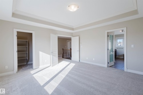 Unfurnished bedroom featuring a walk in closet, light carpet, ornamental molding, ensuite bath, and a raised ceiling - 3612 Mclay Court, Edmonton, AB - Indoor