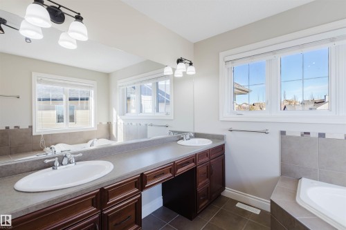Full bathroom with a garden tub, double vanity, hanging lights, dark tile patterned floors, and plenty of natural light - 3612 Mclay Court, Edmonton, AB - Indoor Photo Showing Bathroom