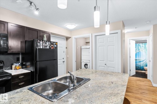 Kitchen featuring decorative light fixtures, black appliances, dark wood finish cabinets, and light wood-style floors - 224 920 156 Street, Edmonton, AB - Indoor Photo Showing Kitchen With Double Sink
