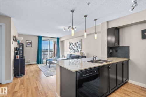 Kitchen featuring dishwasher, dark cabinetry, light stone countertops, a peninsula, and open floor plan - 224 920 156 Street, Edmonton, AB - Indoor Photo Showing Kitchen With Double Sink