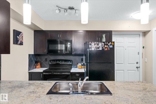 Kitchen featuring black appliances, backsplash, hanging light fixtures, and dark wood finish cabinets - 224 920 156 Street, Edmonton, AB - Indoor Photo Showing Kitchen With Double Sink