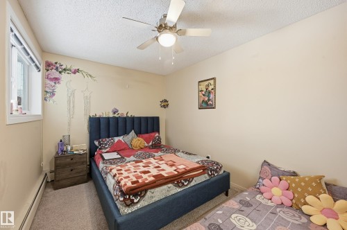 Carpeted bedroom featuring baseboard heating, a ceiling fan, and a textured ceiling - 302 2624 Mill Woods Road E, Edmonton, AB - Indoor Photo Showing Bedroom