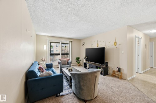 Carpeted living room with a textured ceiling and baseboards - 302 2624 Mill Woods Road E, Edmonton, AB - Indoor