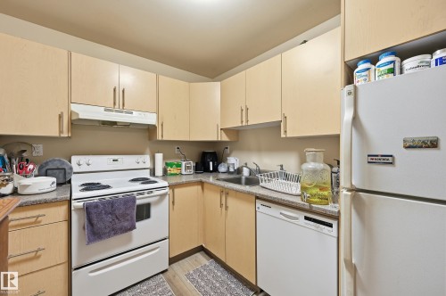 Kitchen featuring white appliances, light wood finish cabinetry, light countertops, and light wood-style floors - 302 2624 Mill Woods Road E, Edmonton, AB - Indoor Photo Showing Kitchen