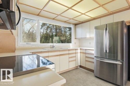 Two tone kitchen featuring stainless steel appliances, light countertops, decorative backsplash, light floors, and two tone cabinetry - 14335 47 Avenue, Edmonton, AB - Indoor Photo Showing Kitchen