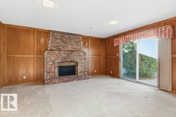 Unfurnished living room with light colored carpet, a brick fireplace, and wooden walls - 