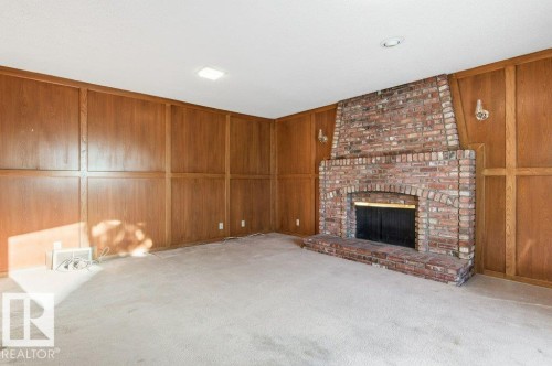 Unfurnished living room with wood walls, light colored carpet, and a brick fireplace - 14335 47 Avenue, Edmonton, AB - Indoor With Fireplace
