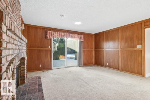 Unfurnished living room featuring a fireplace, light colored carpet, a textured ceiling, and wood walls - 14335 47 Avenue, Edmonton, AB - Indoor Photo Showing Other Room
