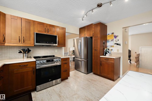 Kitchen featuring stainless steel appliances, wood finish cabinets, tasteful backsplash, a textured ceiling, and rail lighting - 9804 156 Avenue, Edmonton, AB - Indoor Photo Showing Kitchen With Stainless Steel Kitchen
