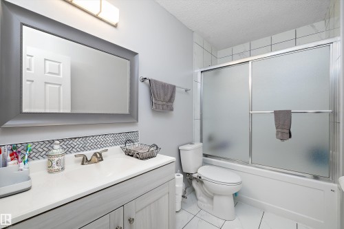 Full bathroom with vanity, enclosed tub / shower combo, a textured ceiling, and tasteful backsplash - 9804 156 Avenue, Edmonton, AB - Indoor Photo Showing Bathroom