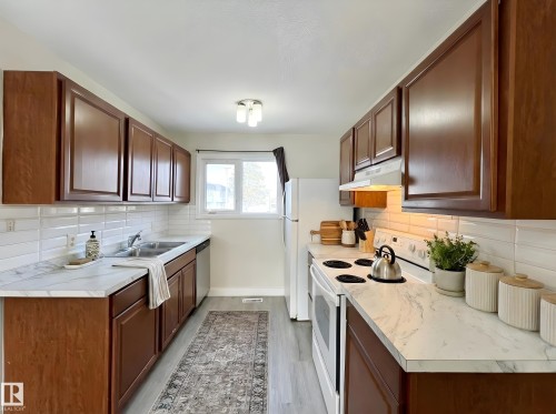 Kitchen with white appliances, light countertops, backsplash, and light wood-style floors - 11357 22 Avenue, Edmonton, AB - Indoor Photo Showing Kitchen With Double Sink