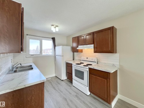 Kitchen with white appliances, light countertops, decorative backsplash, light wood-style floors, and a textured ceiling - 11357 22 Avenue, Edmonton, AB - Indoor Photo Showing Kitchen With Double Sink