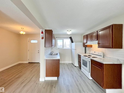 Kitchen featuring white appliances, light countertops, backsplash, light wood-style flooring, and a textured ceiling - 11357 22 Avenue, Edmonton, AB - Indoor Photo Showing Kitchen With Double Sink
