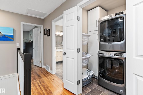 Laundry area with attic access, cabinet space, stacked washer / drying machine, and wood finished floors - 317 Grand Meadow Crescent, Edmonton, AB - Indoor Photo Showing Laundry Room