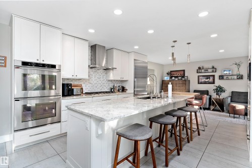 Kitchen with stainless steel appliances, a center island with sink, light stone counters, white cabinets, and a kitchen breakfast bar - 317 Grand Meadow Crescent, Edmonton, AB - Indoor Photo Showing Kitchen With Upgraded Kitchen
