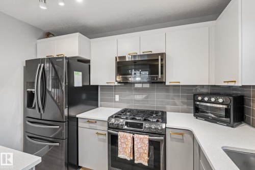 Dual tone kitchen with stainless steel appliances, gas stove, a kitchen island, light wood-type flooring, decorative backsplash, and dual tone cabinetry - 89 Hewitt Circle, Spruce Grove, AB - Indoor Photo Showing Kitchen