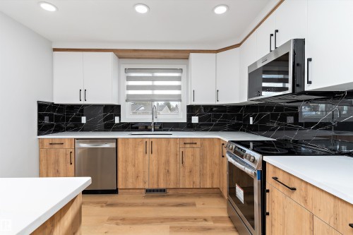 Two tone kitchen featuring two tone cabinets, stainless steel appliances, light wood finished floors, modern cabinets, and light stone countertops - 17116 81 Avenue, Edmonton, AB - Indoor Photo Showing Kitchen