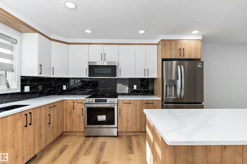 Kitchen with two tone cabinetry, stainless steel appliances, light wood finished floors, light stone countertops, and tasteful backsplash - 17116 81 Avenue, Edmonton, AB - Indoor Photo Showing Kitchen