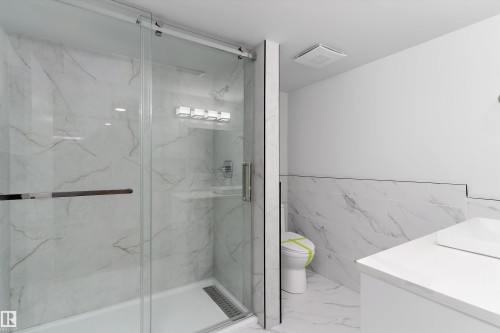 Full bath featuring tile walls, a marble finish shower, vanity, a wainscoted wall, and light marble finish flooring - 17116 81 Avenue, Edmonton, AB - Indoor Photo Showing Bathroom