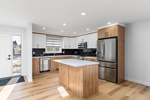 Kitchen featuring two tone cabinets, stainless steel appliances, backsplash, light wood-type flooring, and a center island - 17116 81 Avenue, Edmonton, AB - Indoor Photo Showing Kitchen