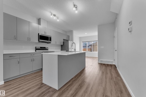 Kitchen featuring stainless steel appliances, light wood finished floors, a kitchen island with sink, gray cabinetry, and a textured ceiling - 1235 16 Avenue, Edmonton, AB - Indoor Photo Showing Kitchen With Upgraded Kitchen