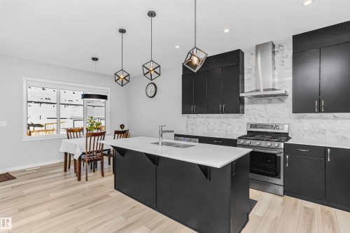 Kitchen featuring dark cabinets, decorative light fixtures, gas stove, a kitchen island with sink, and light wood-type flooring - 3108 158 Street, Edmonton, AB - Indoor Photo Showing Kitchen With Double Sink