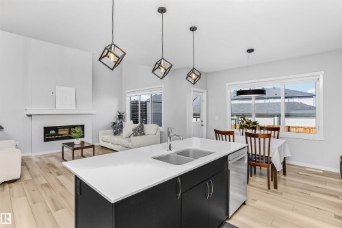 Kitchen featuring dark cabinetry, pendant lighting, a fireplace, light wood finished floors, and a center island with sink - 3108 158 Street, Edmonton, AB - Indoor With Fireplace