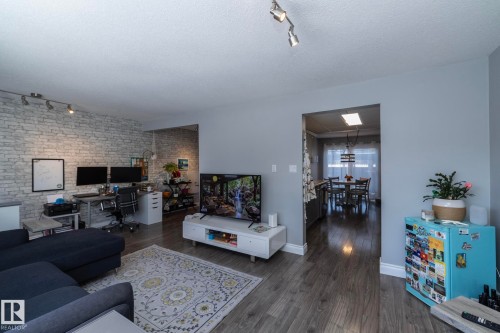 Living room with rail lighting, an office area, dark wood finished floors, a textured ceiling, and brick wall - 4371 46 Street, Stony Plain, AB - Indoor Photo Showing Living Room