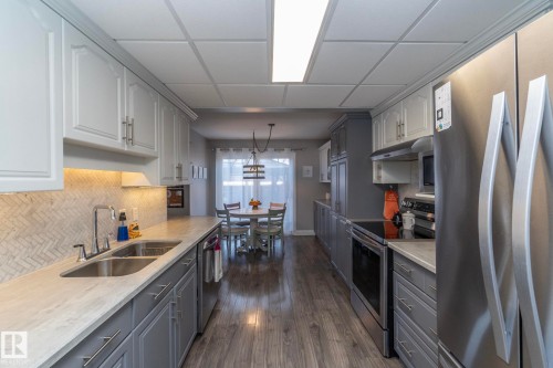 Kitchen featuring stainless steel appliances, decorative light fixtures, dark wood-style floors, a drop ceiling, and gray cabinets - 4371 46 Street, Stony Plain, AB - Indoor Photo Showing Kitchen With Double Sink