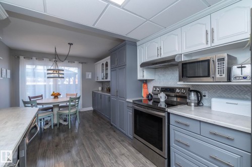 Two tone kitchen featuring stainless steel appliances, two tone cabinetry, dark wood-type flooring, hanging light fixtures, and decorative backsplash - 4371 46 Street, Stony Plain, AB - Indoor Photo Showing Kitchen