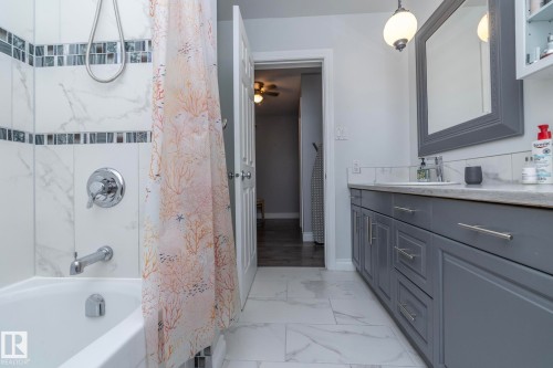 Full bathroom featuring shower / bath combination with curtain, light marble finish flooring, vanity, and ceiling fan - 4371 46 Street, Stony Plain, AB - Indoor Photo Showing Bathroom