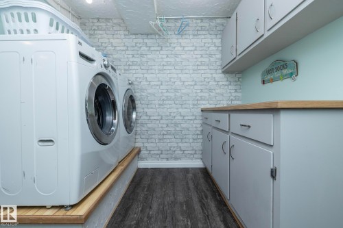 Laundry room with brick wall, cabinet space, dark wood-style floors, and washing machine and dryer - 4371 46 Street, Stony Plain, AB - Indoor Photo Showing Laundry Room