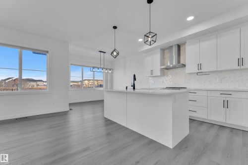 Kitchen featuring white cabinetry, decorative backsplash, decorative light fixtures, a kitchen island with sink, and light stone countertops - 1822 Collip View View, Edmonton, AB - Indoor Photo Showing Kitchen With Upgraded Kitchen