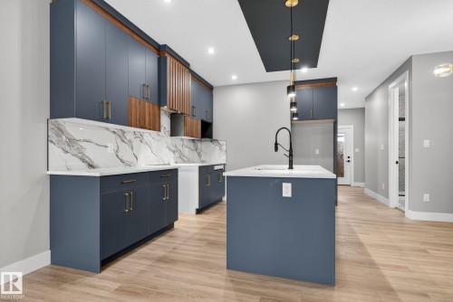 Kitchen featuring modern cabinets, an island with sink, light stone countertops, light wood-style floors, and decorative light fixtures - 456 Crystal Creek Link, Leduc, AB - Indoor Photo Showing Kitchen With Upgraded Kitchen