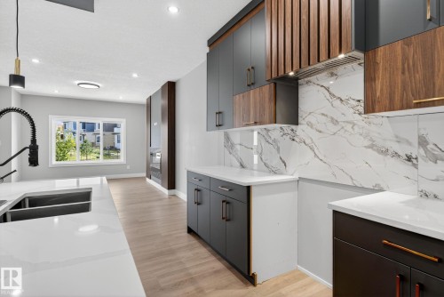 Dual tone kitchen featuring light stone countertops, light wood finished floors, two tone cabinetry, modern cabinets, and decorative backsplash - 456 Crystal Creek Link, Leduc, AB - Indoor Photo Showing Kitchen With Double Sink